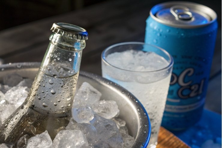 Chilled glass beverage bottle in ice bucket with soda can and iced glass