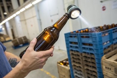 Handheld flashlight checks amber bottle clarity and defects on production floor