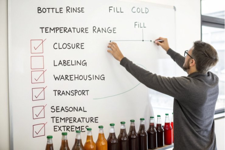 Technician checks bottling process steps on whiteboard with filled glass bottles below