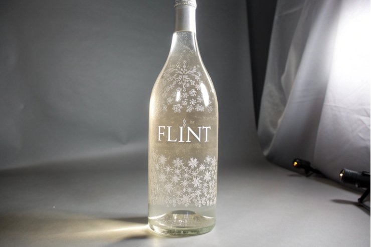 Clear frosted wine bottle with floral etching and FLINT branding on studio backdrop