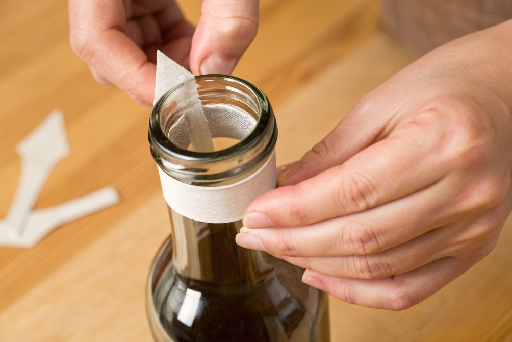 Hands applying tamper evident neck label to dark glass bottle
