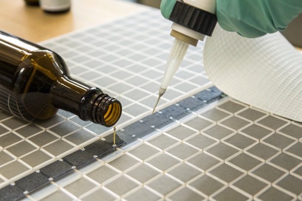Gloved hand dispensing liquid onto grid while testing amber bottle leak and residue