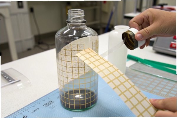 Hand applying label grid to glass bottle for measurement and compliance checks