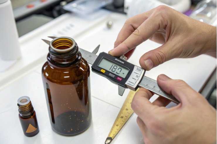 Technician measuring amber bottle neck diameter with digital caliper in quality control lab