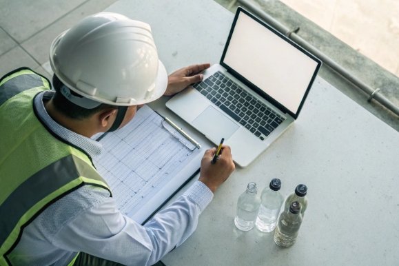 Quality engineer records test data with laptop beside sample glass bottles