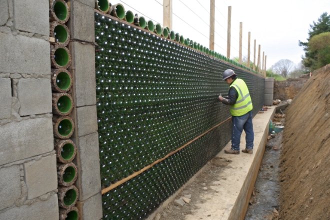 Worker building retaining wall using recycled glass bottles embedded in concrete