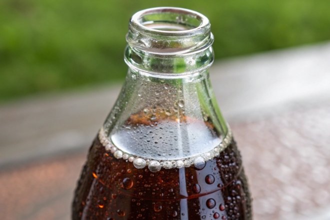 Clear glass soda bottle neck with condensation and carbonation bubbles outdoors