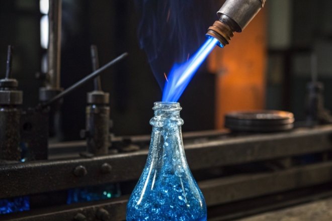 Blue glass bottle neck heated by flame torch during forming process on production line