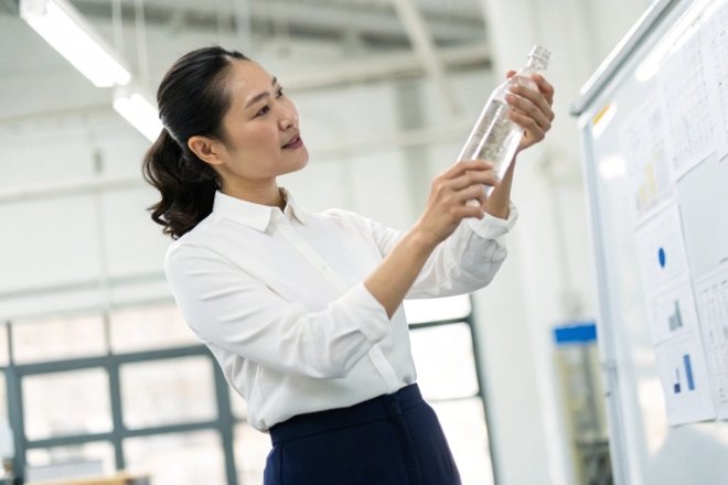 Quality inspector examining clear glass bottle under factory lighting