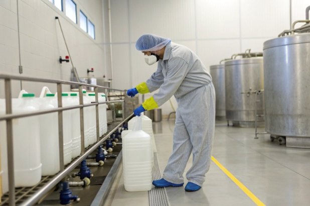 Worker handling large plastic containers on industrial filling line in hygienic facility