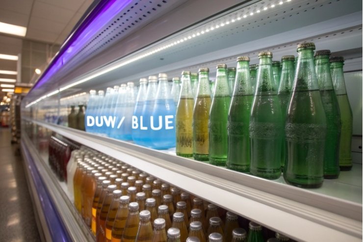 Refrigerated retail shelf with green glass soda bottles and assorted beverages