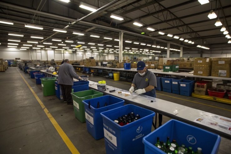 Workers sort returned glass bottles into bins on recycling line inside facility