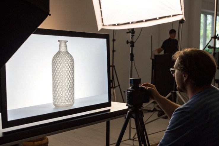 Studio photographer capturing patterned glass bottle with softbox lighting and camera rig