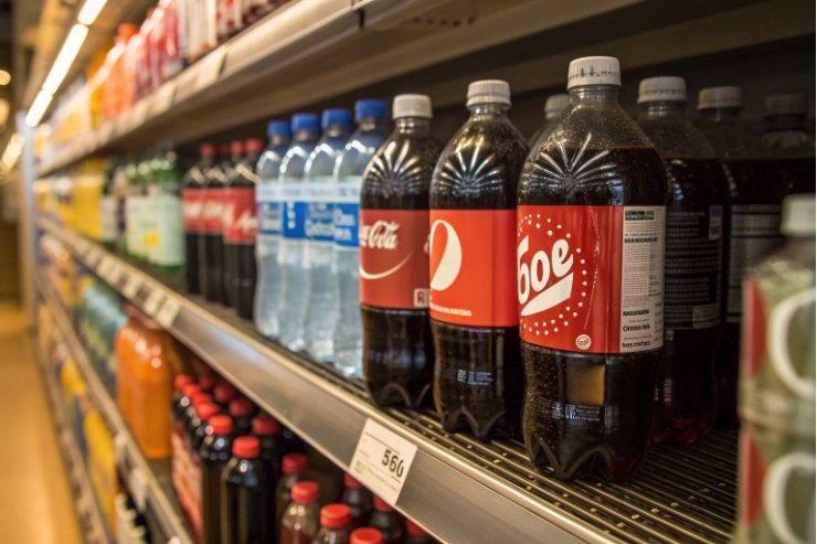 Supermarket shelf stocked with plastic cola bottles and bottled water soft drinks