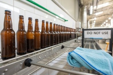 Cleaned amber bottles lined on conveyor beside 'do not use' sign and towel