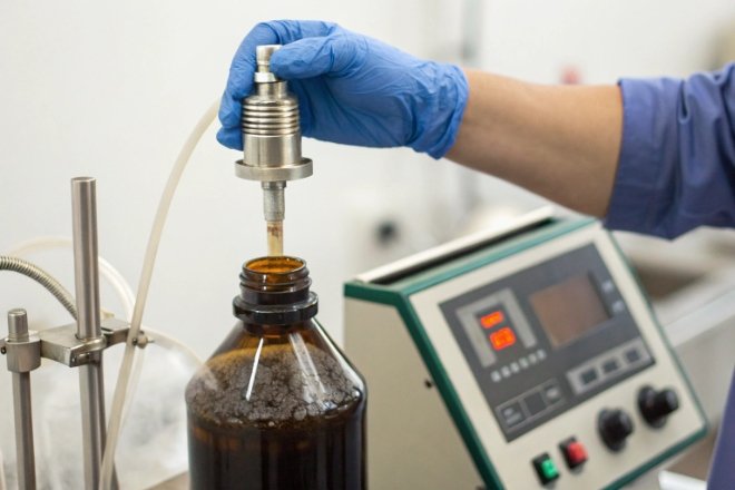 Gloved technician testing amber bottle with probe and instrument panel for quality control