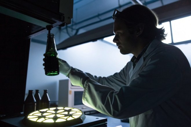 Lab technician inspecting green glass bottle under light for defect and clarity control