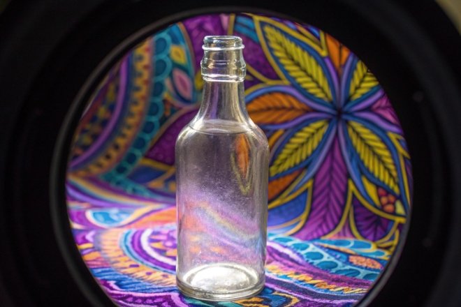 Clear glass bottle framed by circular view with colorful patterned background for inspection