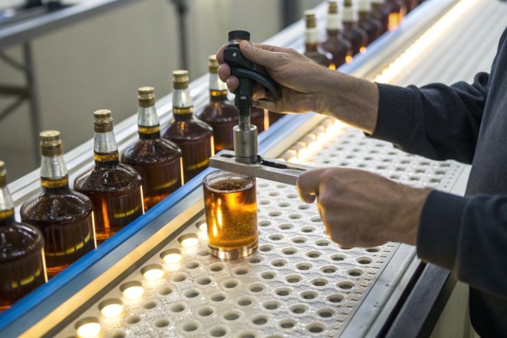 Quality inspection measuring filled liquor bottle on bottling line with sealed glass bottles behind