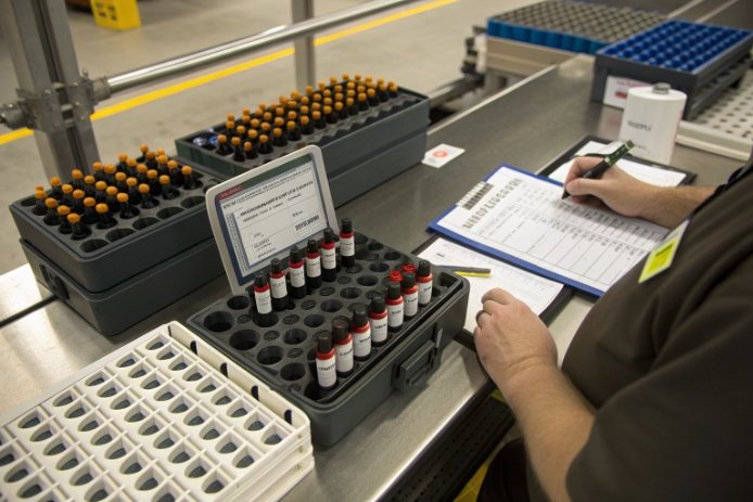 Quality inspector recording sample tests for small bottles and vials on production line
