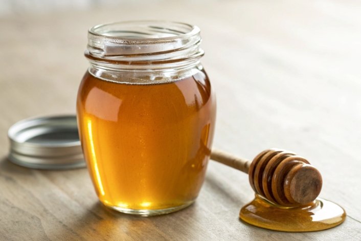 clear glass honey jar with golden honey and wooden dipper