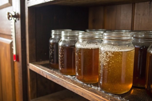 glass jars of honey stored on wooden pantry shelf at room temperature