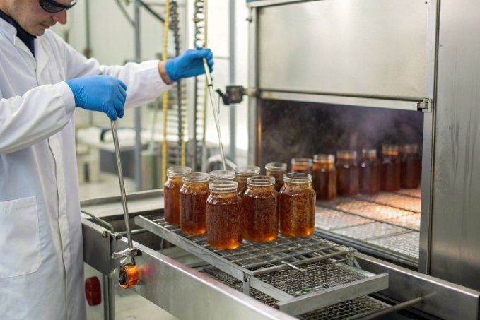 lab technician heat treating filled glass jars in industrial sterilization oven