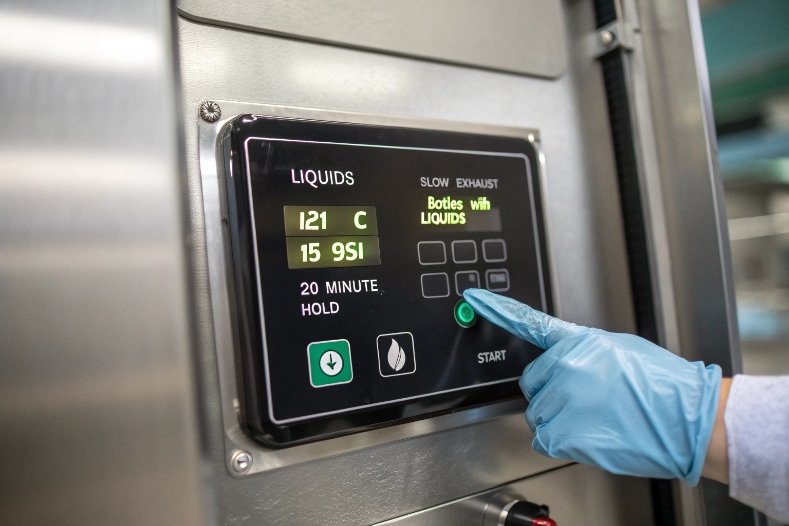 Gloved technician setting temperature on stainless steel autoclave control panel for liquids