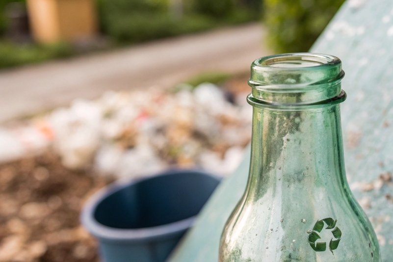 green recycled glass bottle with recycling symbol in outdoor collection area