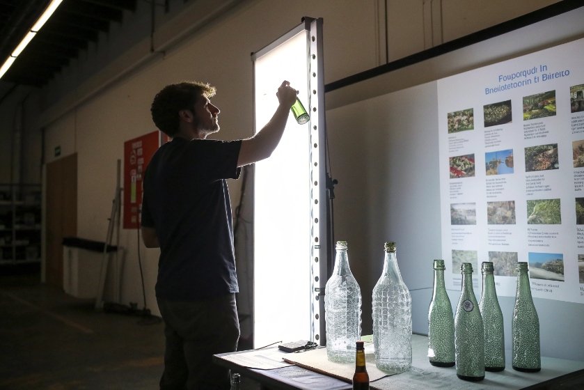Technician inspecting green glass bottle under backlight with sample bottles on table