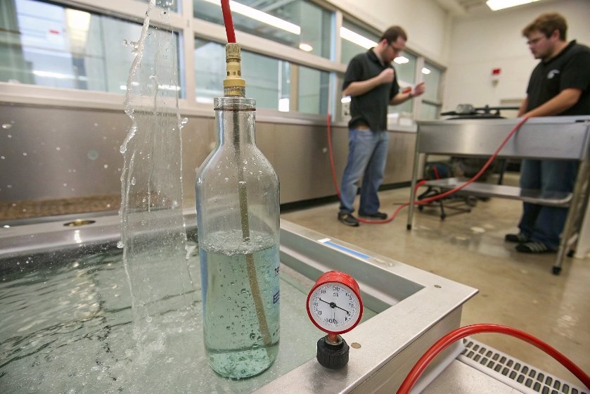 Laboratory pressure test on glass bottle submerged in water with gauge and technicians