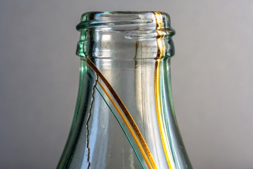 Closeup of glass bottle neck showing vertical crack and stress pattern lines