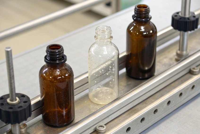 three small glass bottles on conveyor for cosmetic or pharmaceutical production testing