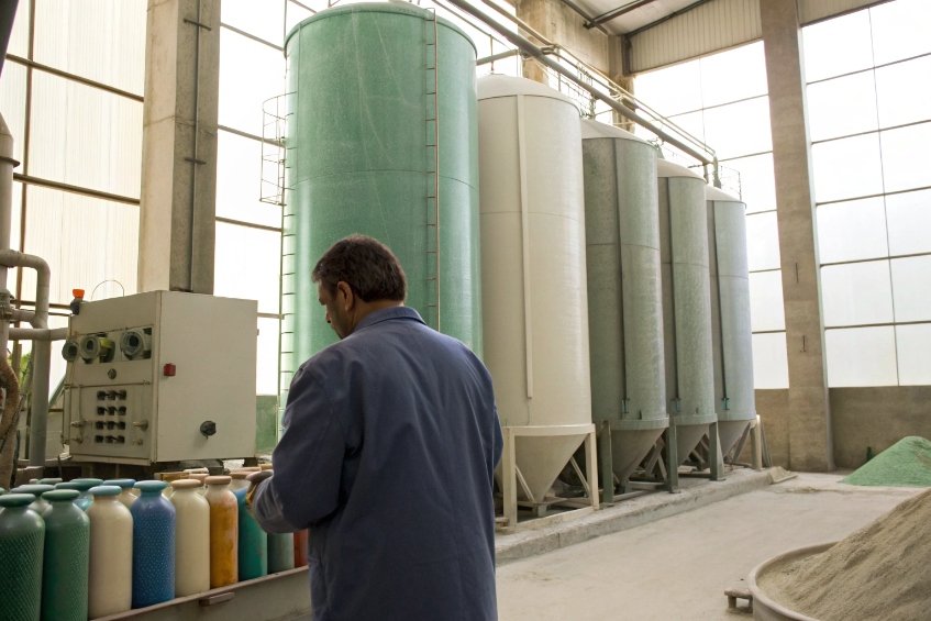 operator checking colored glass raw material containers near large silos