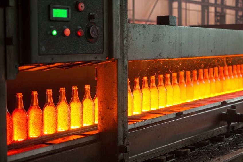row of glowing hot glass bottles in furnace on manufacturing conveyor line