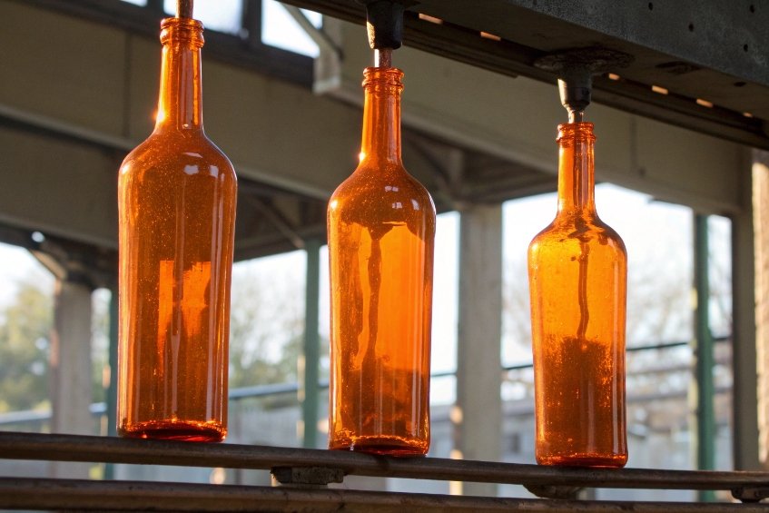 three freshly formed amber glass bottles hanging from overhead cooling conveyor
