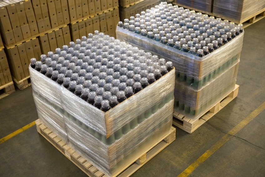 two large pallets of shrink-wrapped bottles stacked on wooden skids in warehouse