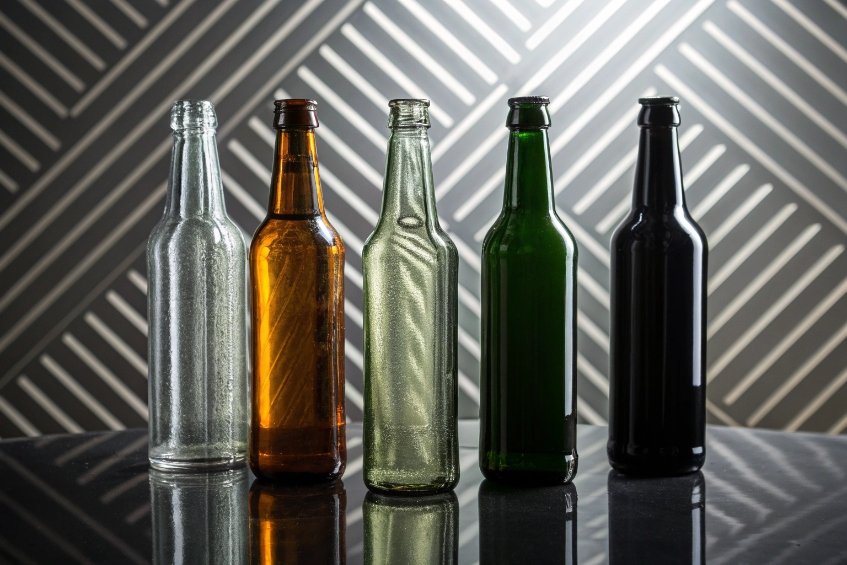 Assorted empty glass beer bottles in different colors standing against geometric background