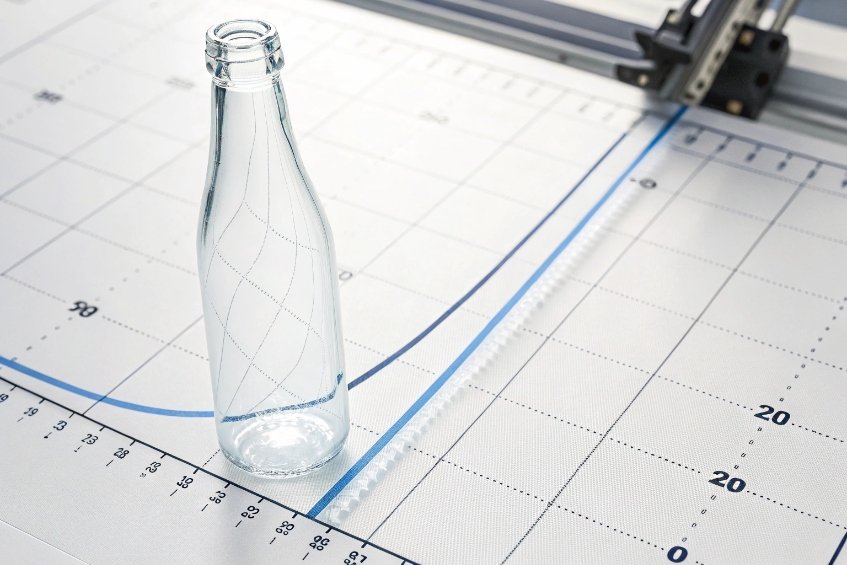 Clear beverage glass bottle standing on technical drawing board for size and design measurement