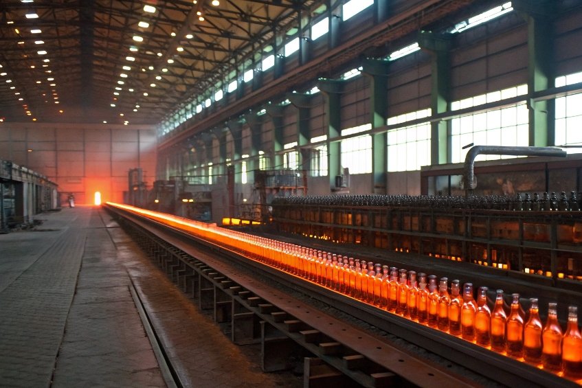 Long annealing lehr with glowing hot glass bottles in large FuSenglass production workshop