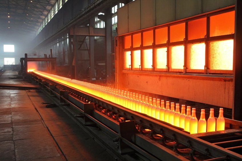 Row of glowing hot glass bottles moving through industrial annealing furnace line