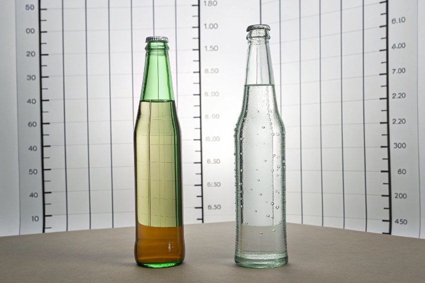 Green and clear beverage glass bottles for capacity measurement in front of calibration chart background