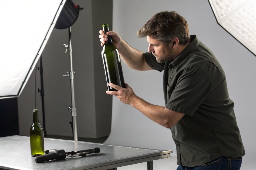 Man inspecting green wine bottle under studio lighting on metal table