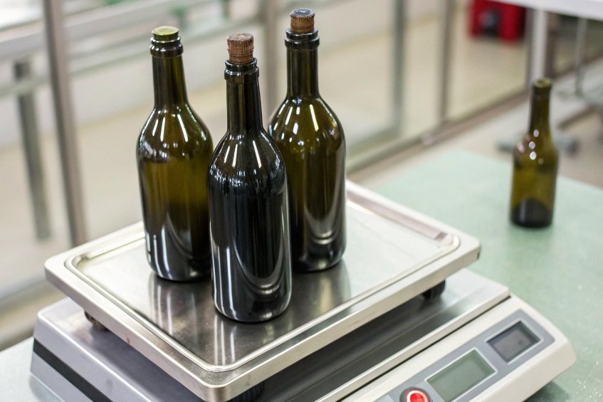 Three filled green wine bottles standing on digital weighing scale in bottling facility