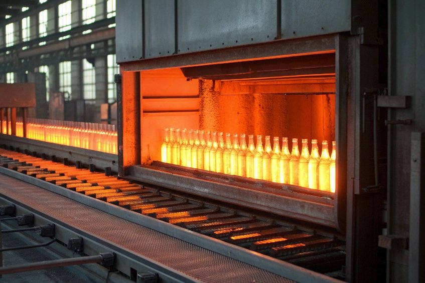Row of glowing hot glass bottles moving through industrial annealing furnace line