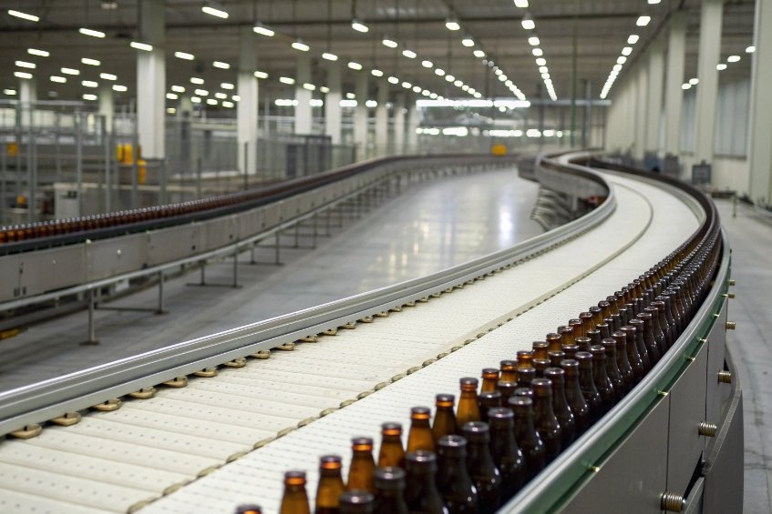 Endless brown beer bottles traveling on curved conveyor in large bottling plant